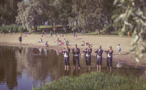 Ryhmä Kuopion kaupunginorkesterin muusikkoja soittamassa jalat vedessä Väinölänniemen rannassa.