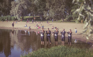 Ryhmä Kuopion kaupunginorkesterin muusikkoja soittamassa jalat vedessä Väinölänniemen rannassa.