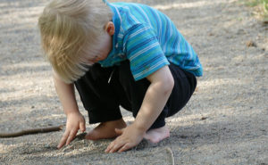 Pieni lapsi piirtelee hiekkaan Kuopion kaupunginorkesterin Suvisoiton aikaan Peräniemellä.