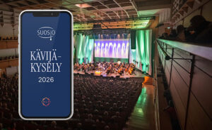 Kävijäkysely-teksti ja orkesteri soittamassa konserttisalin lavalla.